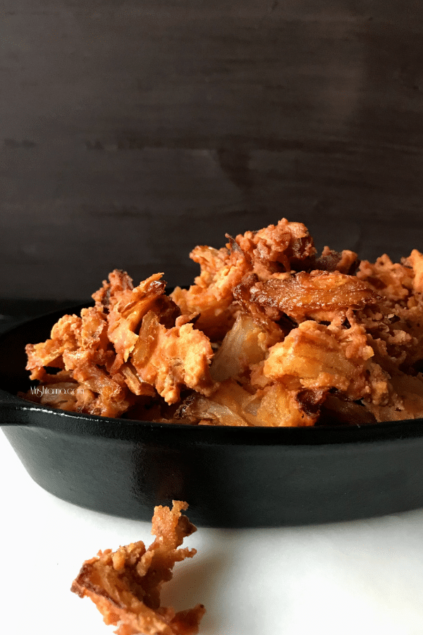 A black cast-iron bowl is filled  with Onion Pakoda