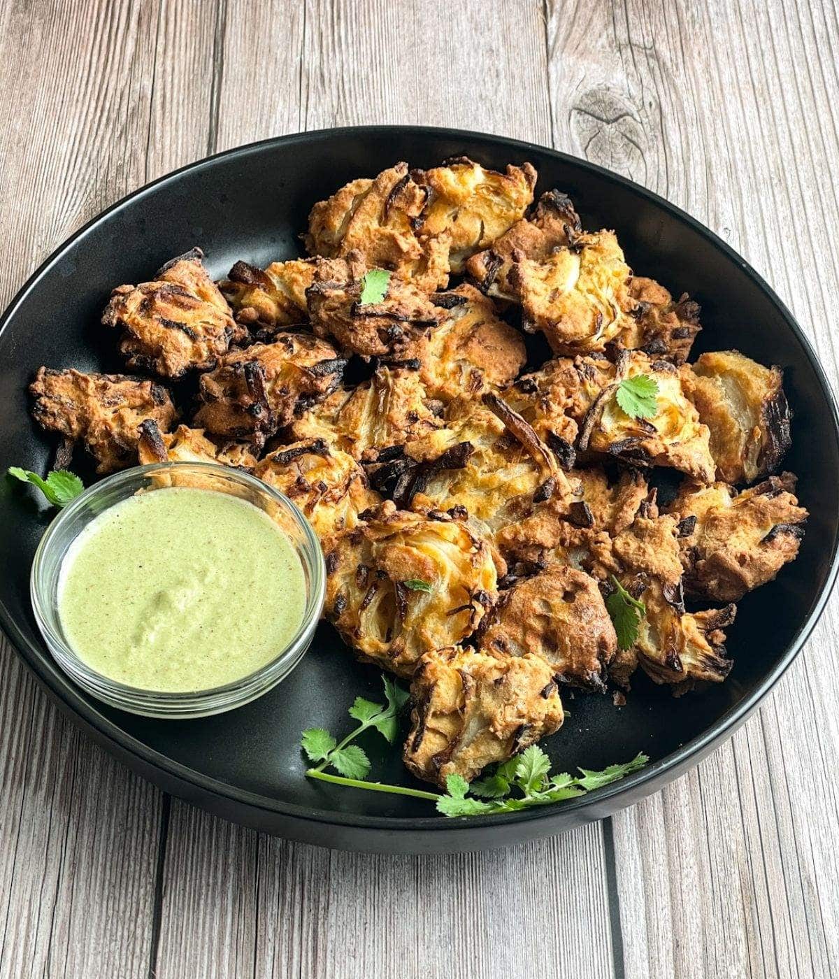 A plate of air fried onion pakodas are on the table with chutney.