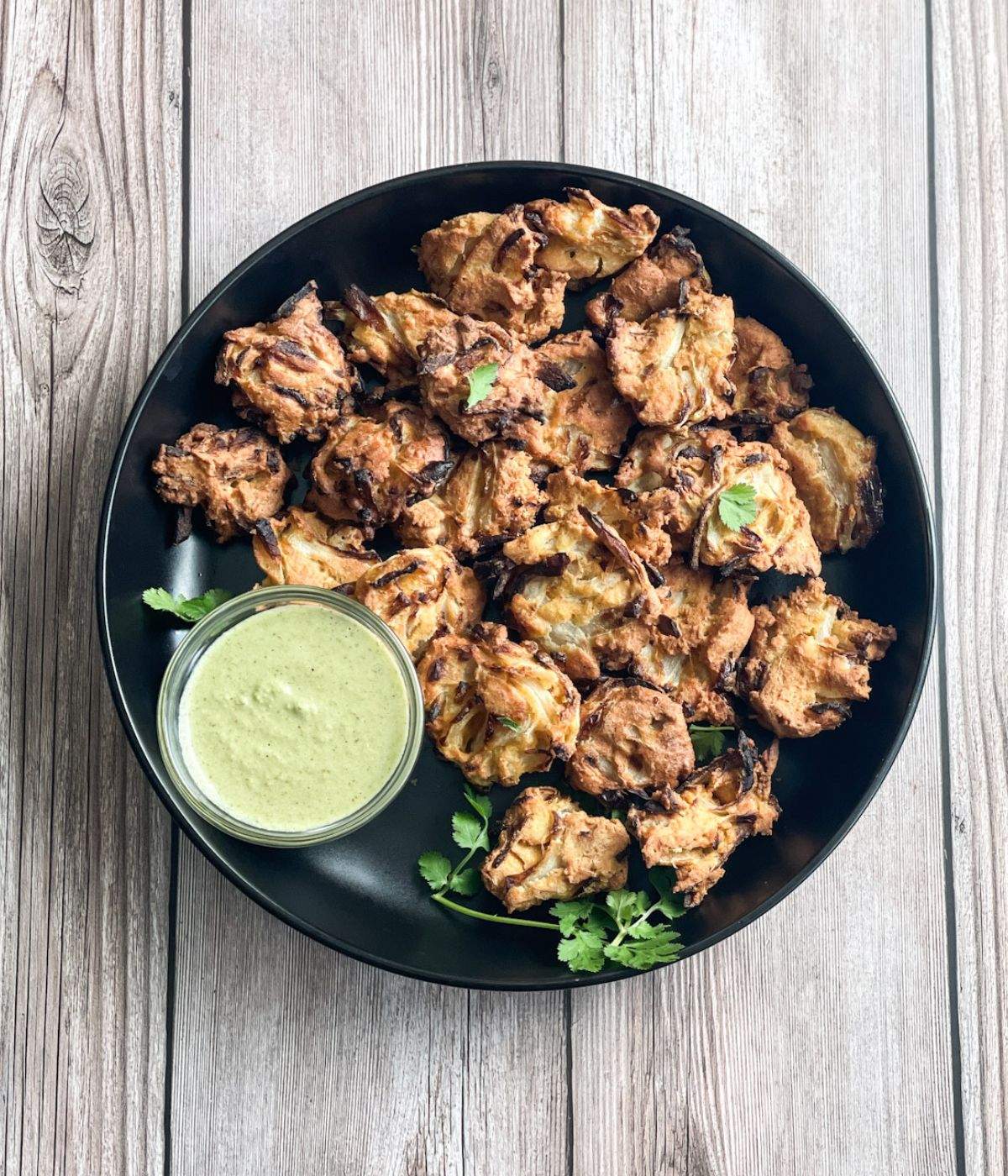 A plate of air fried onion pakodas and chutney is on the table.