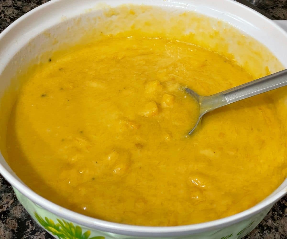 A bowl of aamras or mango rasayana is on the counter top with big spoon.