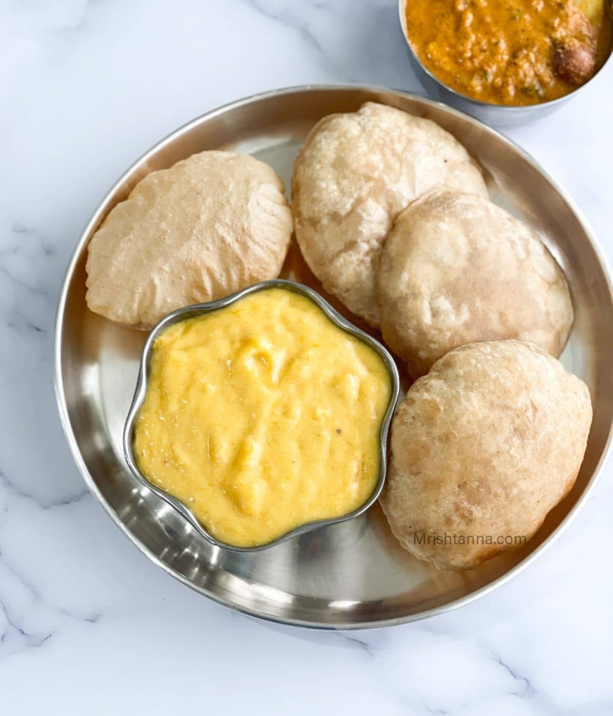 A plate is with Aamras and poori.