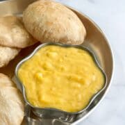 A bowl of aamras is placed on the plate along with pooris.