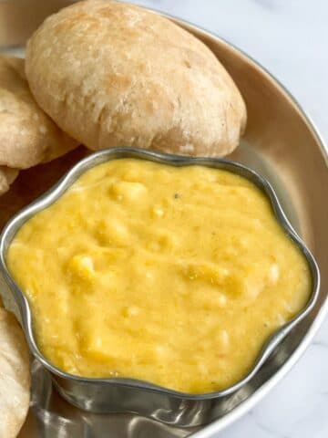 A bowl of aamras is placed on the plate along with pooris.