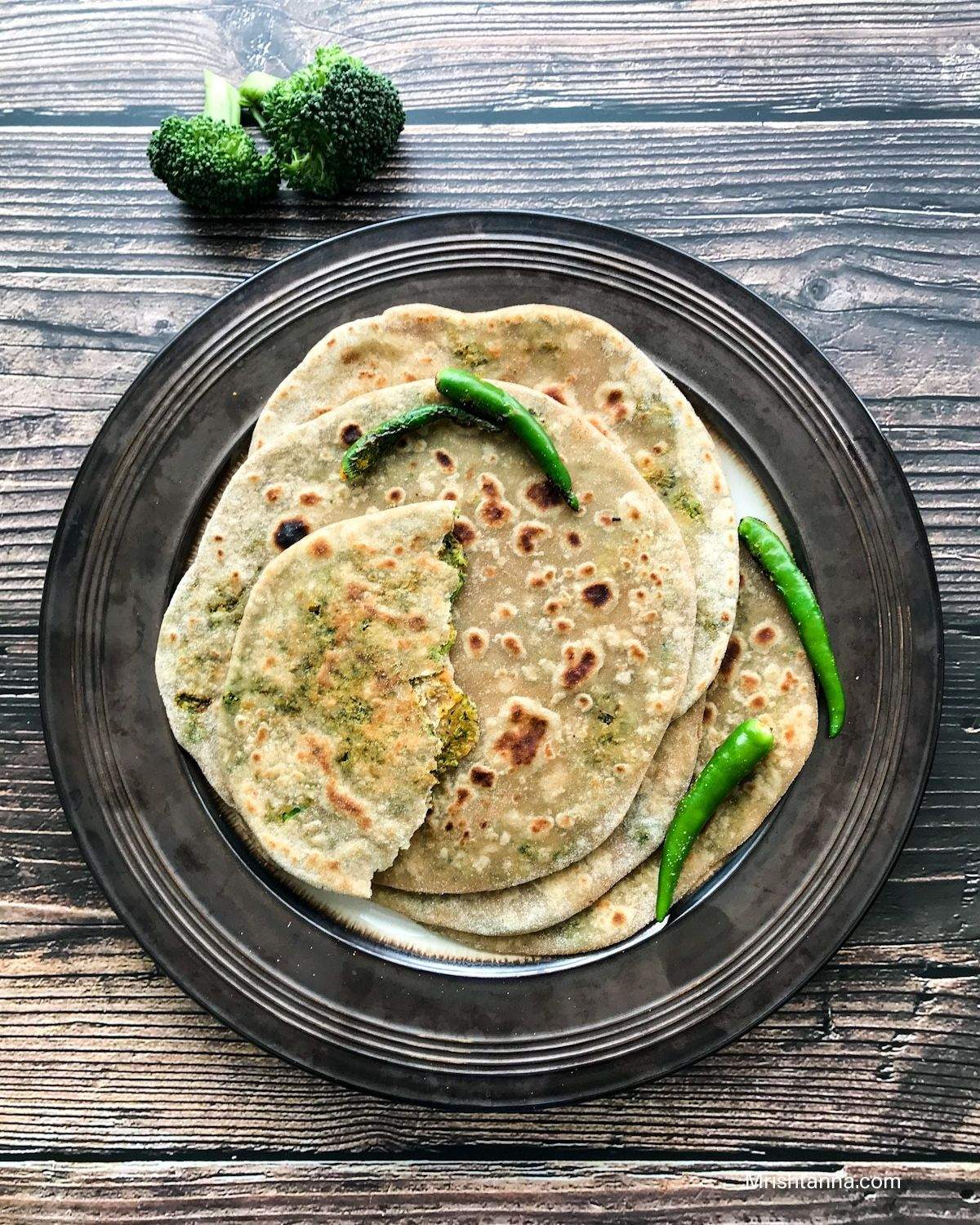 A plate of broccoli paratha and toasted chilies are on the wooden surface