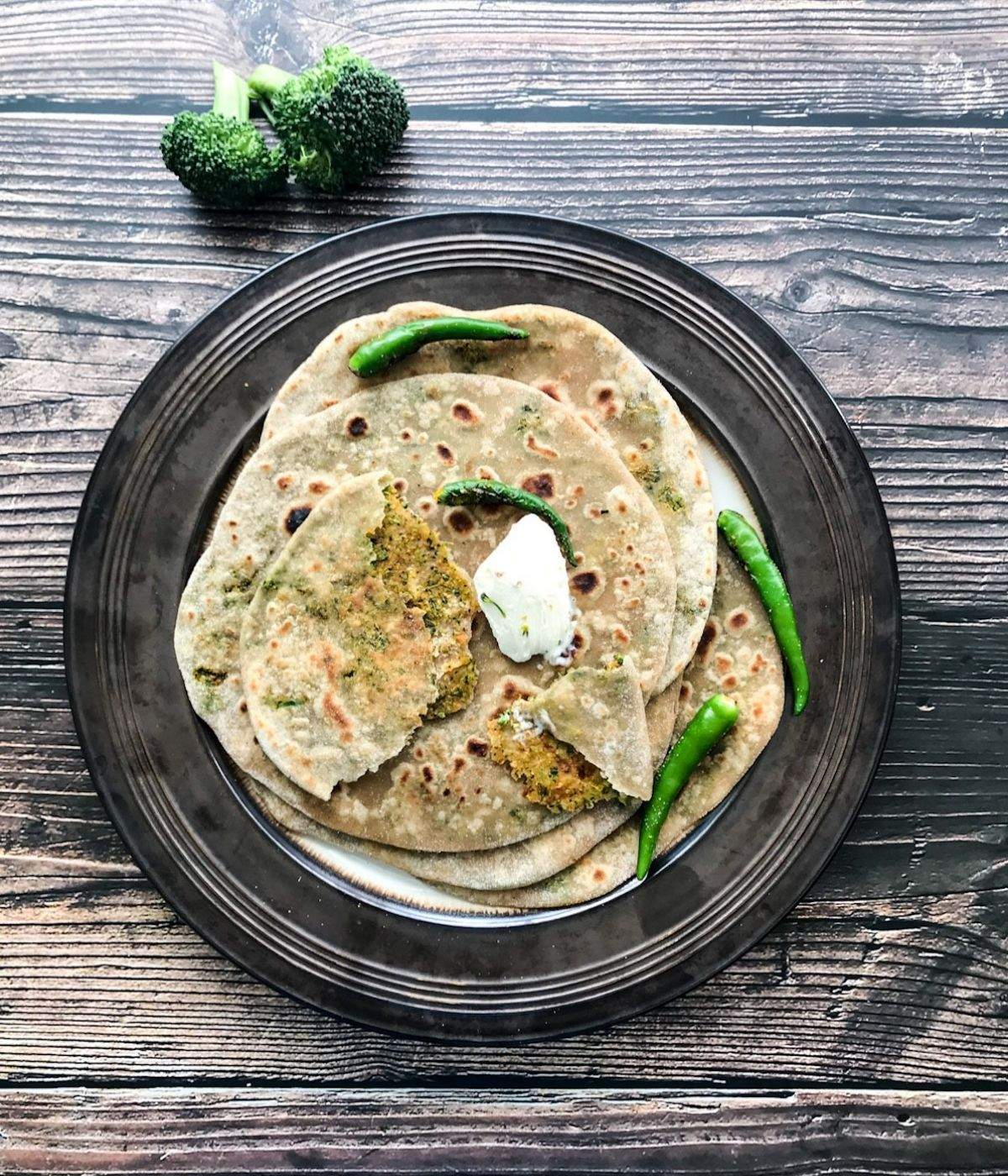 A plate of broccoli paratha os on the table and topped with vegan butter and green chilies