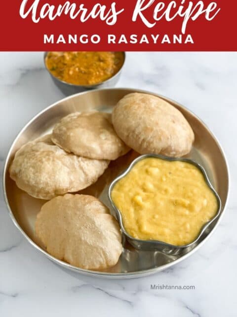 A steel bowl of aamras is on the plate with hot puris.