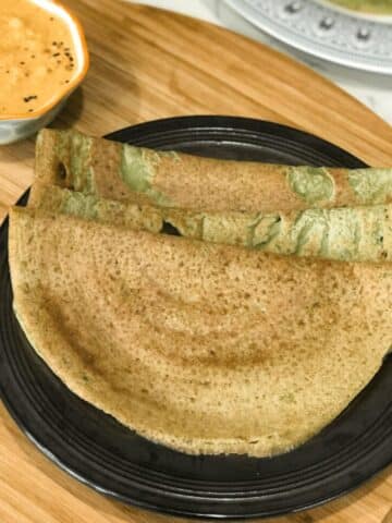 A plate of green gram dosa is on the wooden table with chutney.