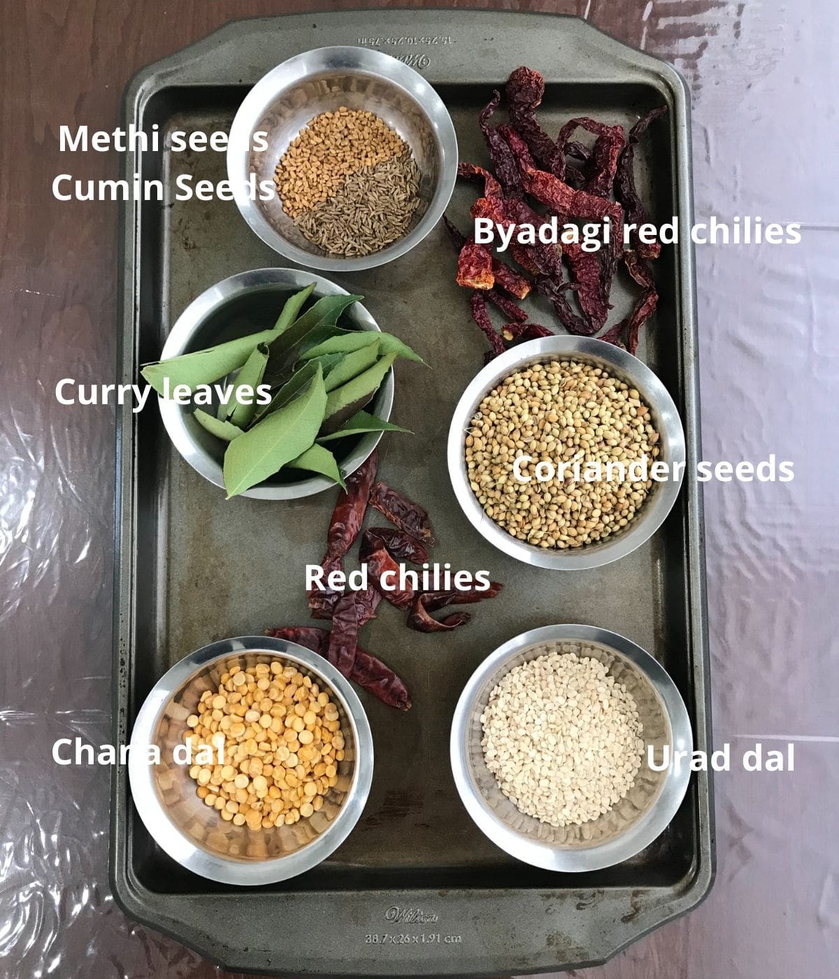 A tray is filled with sambar powder ingredients like red chilies, coriander seeds, and urad dal