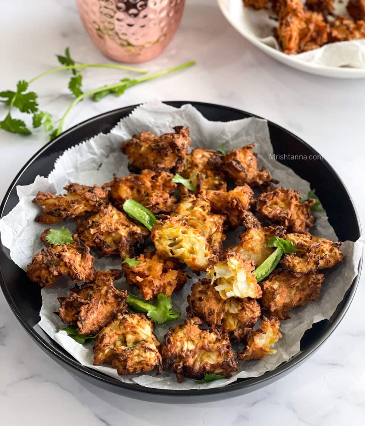 Close up of air fried cabbage pakoras which is placed on the marble table alond with copper mug by the side.