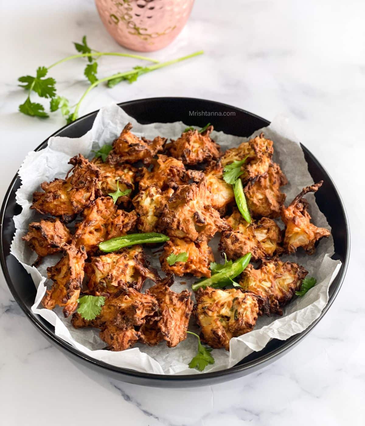 A plate is with air fryer pakora and topped with green chilies and cilantro.