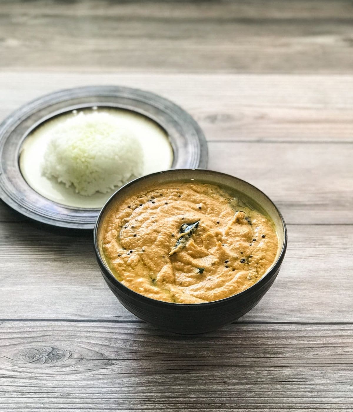 A bowl of cabbage pachadi and plate of rice is on the table