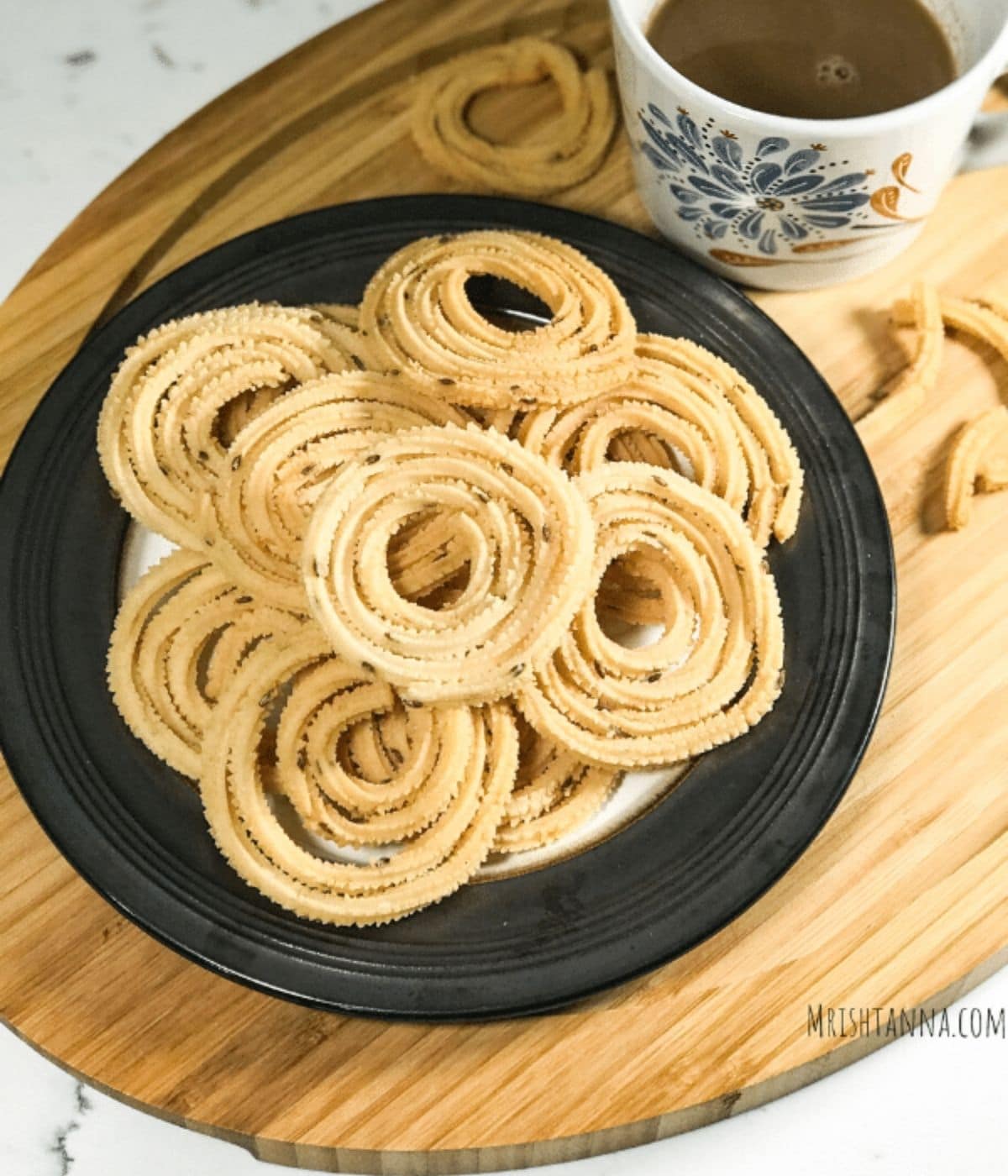 A plate full of chakli is on the table along with cup of coffee.