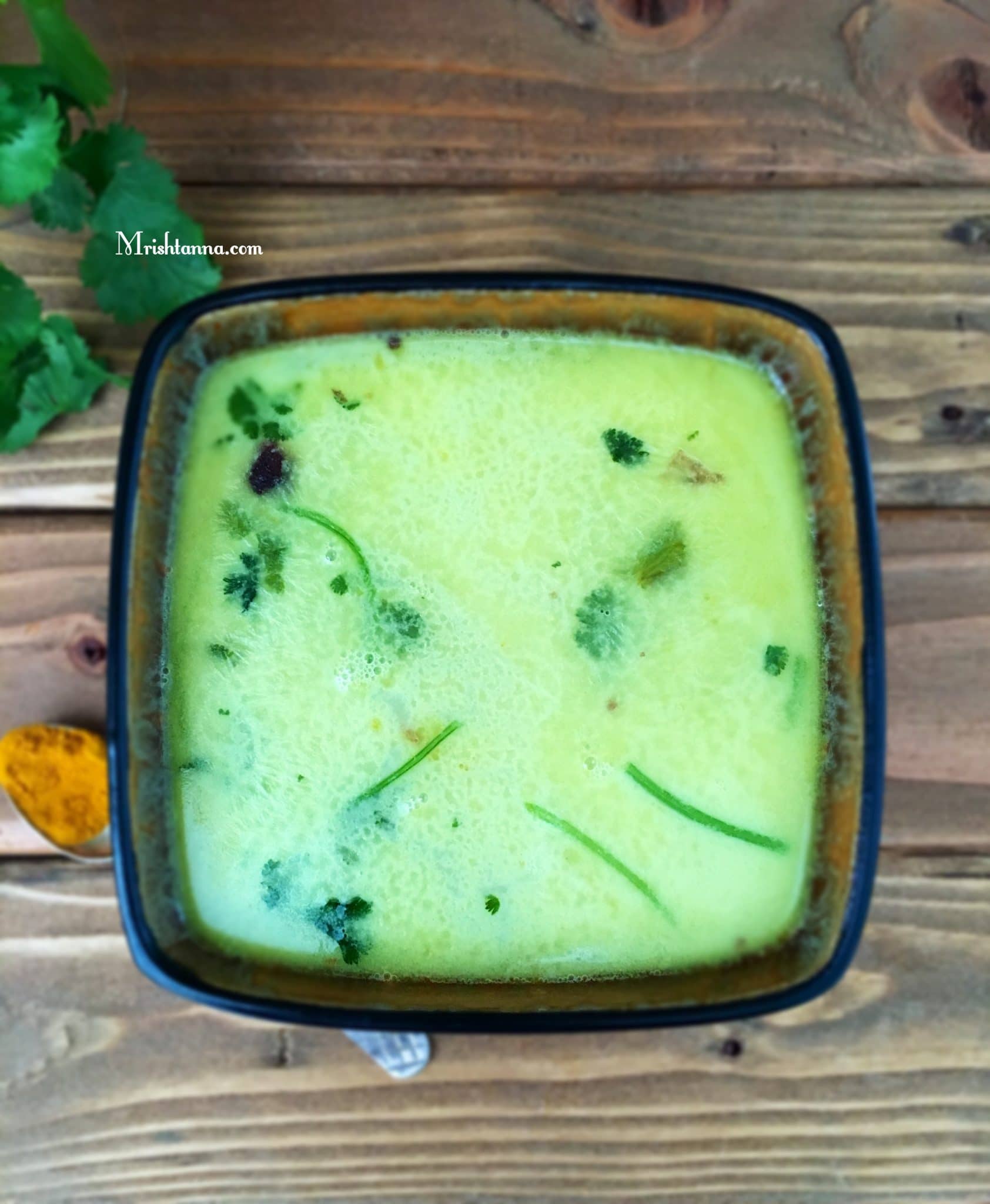 A bowl is filled with moong dal rasam and topped with cilantro