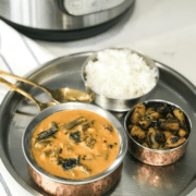 A bowl of sambar on a plate along with rice and stirfry.