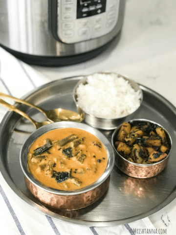 A bowl of sambar on a plate along with rice and stirfry.