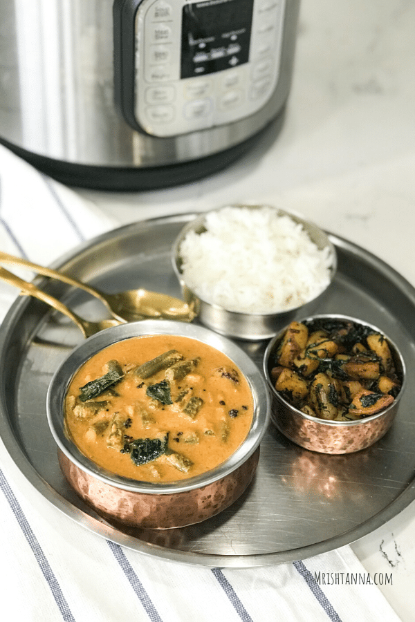A bowl of sambar on a plate along with rice and stirfry.