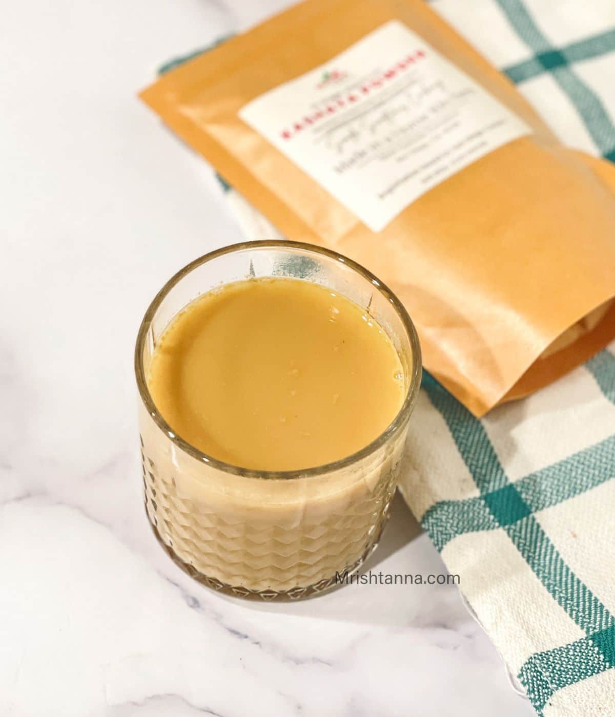 Glass of warm kashayam made using kashaya powder, served on a marble surface with kashaya powder packet in the background.