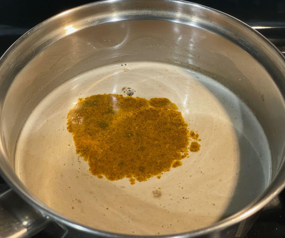 Making kashayam on the stovetop in a stainless steel pot, with the spiced herbal mixture simmering in hot water.