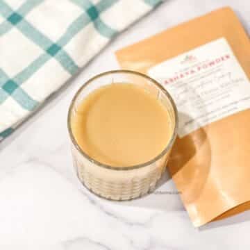 Glass of warm kashayam made using kashaya powder, served on a marble surface with kashaya powder packet in the background.