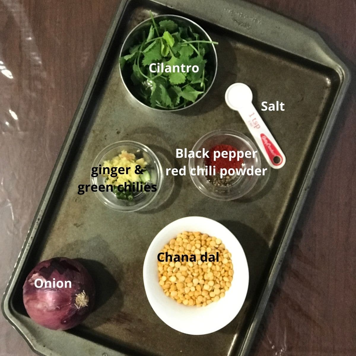 A tray is filled with masala vada ingredients like onions, ginger and chilies