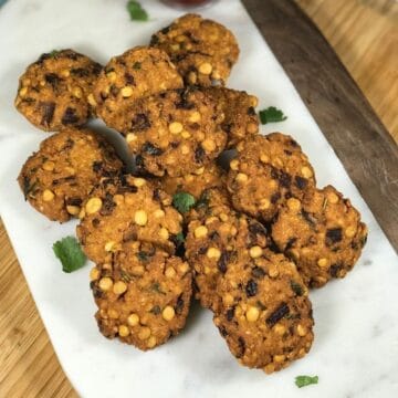 A white tray is filled with masala vadas and bowl of sauce