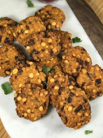 A white tray is filled with masala vadas and bowl of sauce