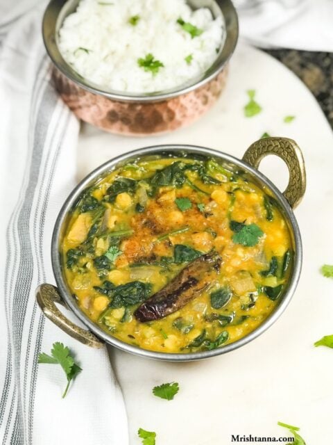 A copper bowl with spinach dal and garnished with tempering and cilantro