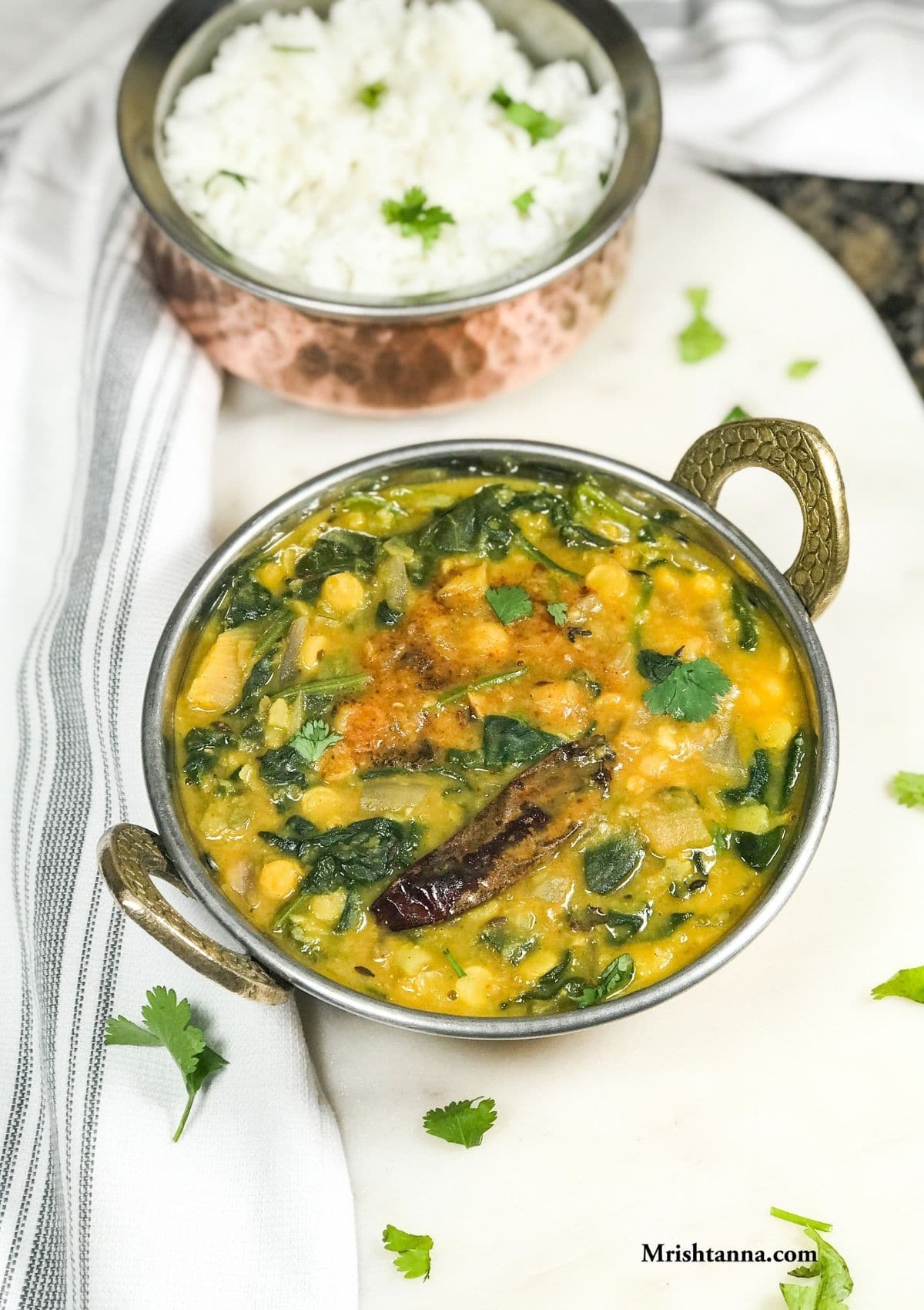 A copper bowl with spinach dal and garnished with tempering and cilantro