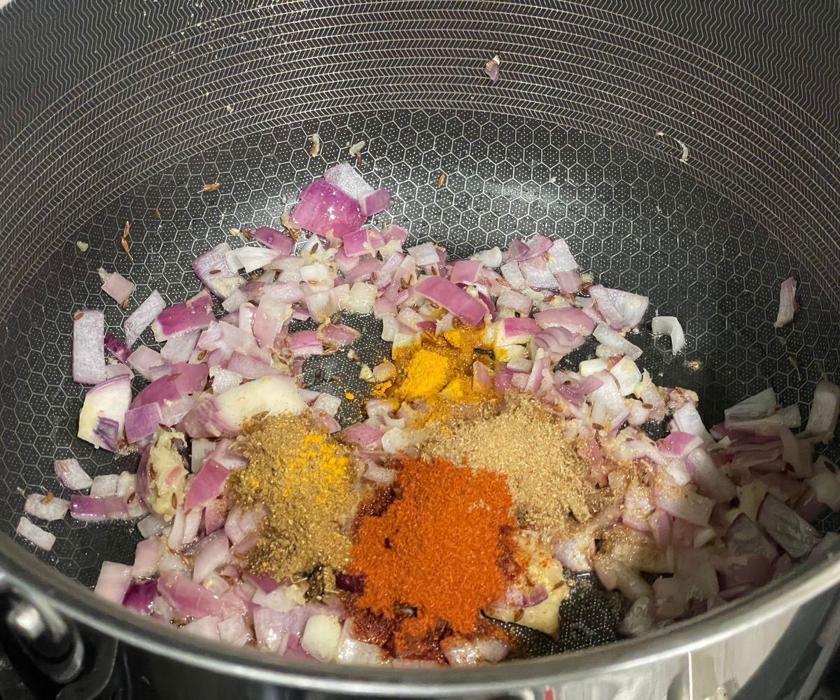 A pan is with spices and onions over the heat.