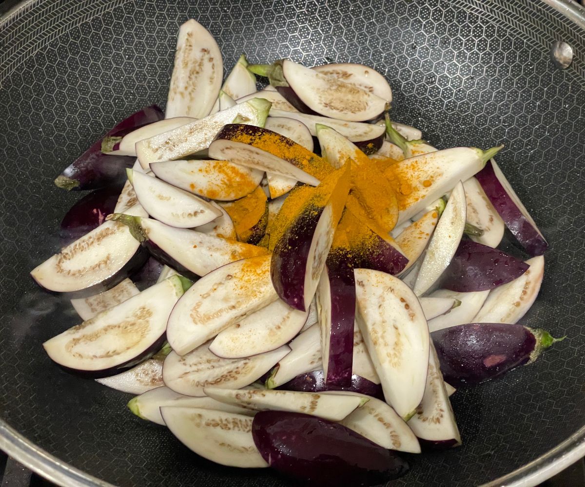 A pan has sliced eggplants and turmeric on the heat.