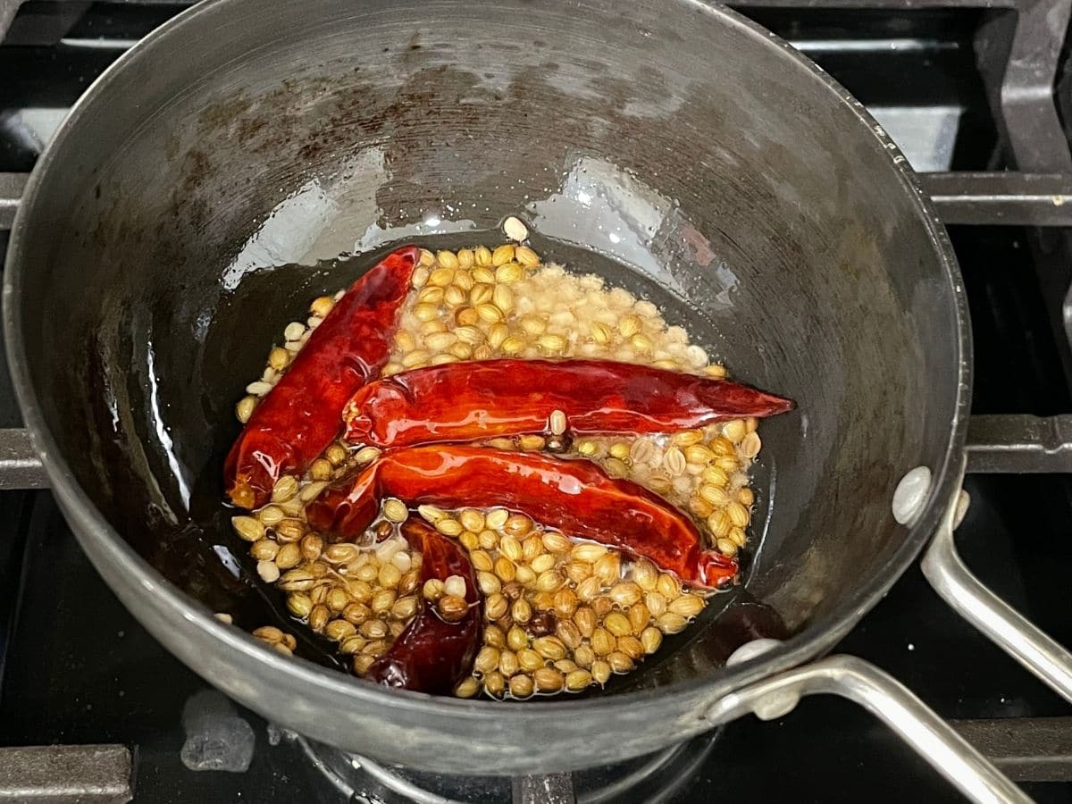 A small pan is with spices and chilies over the heat.