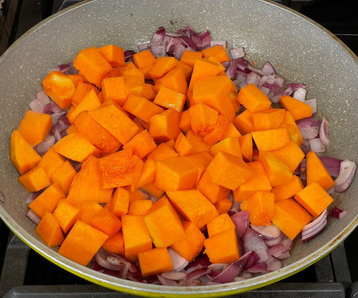 A pan is with spices and pumpkin cubes over the stove top.
