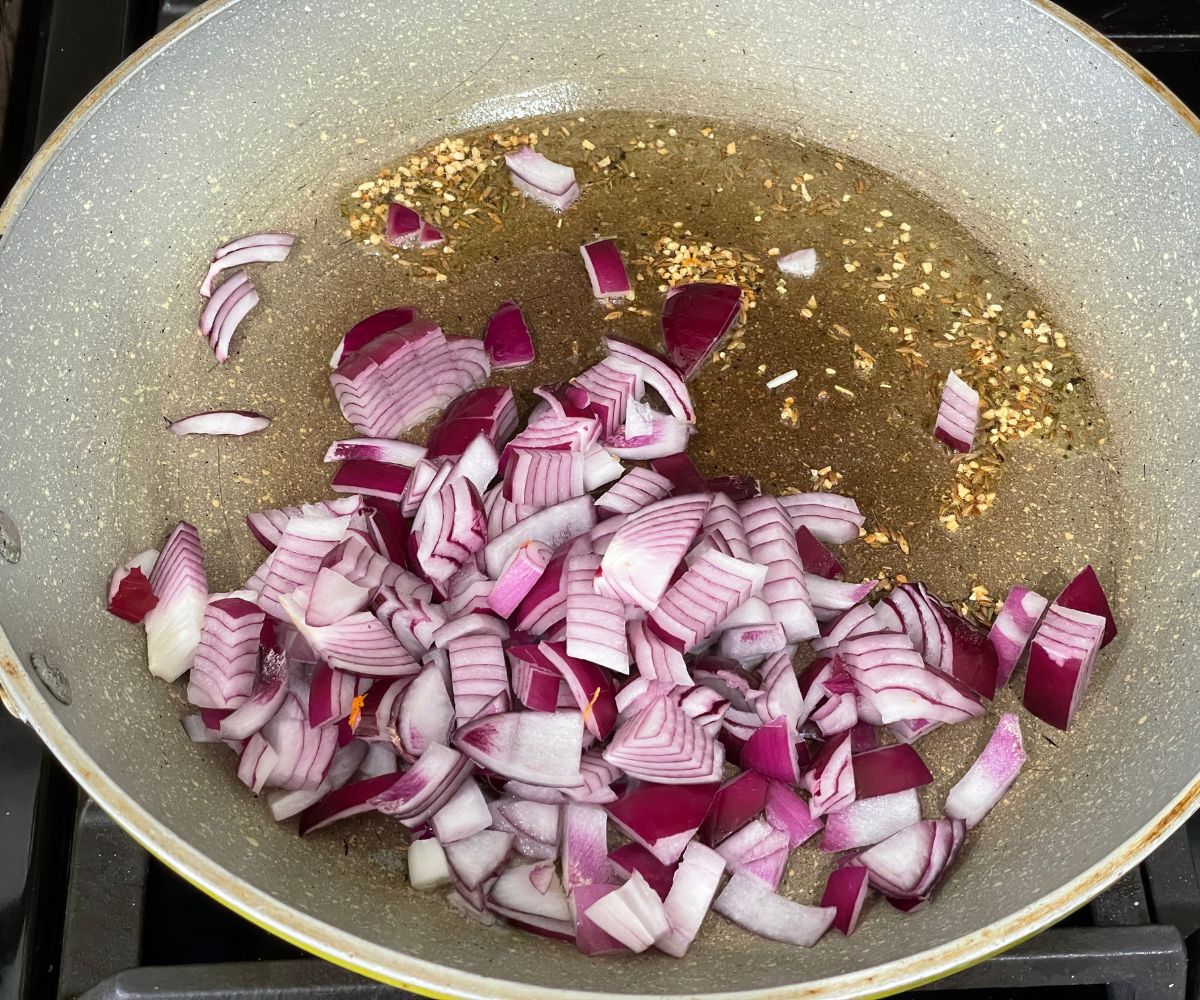 A pan is with cumin seeds, garlic and chopped onions over the heat.