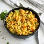 A bowl of pumpkin rice is on the table topped with chopped cilantro.