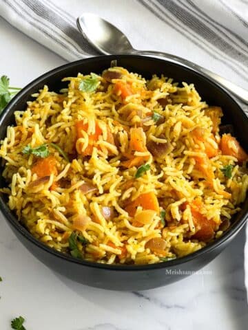 A bowl of pumpkin rice is on the table topped with chopped cilantro.