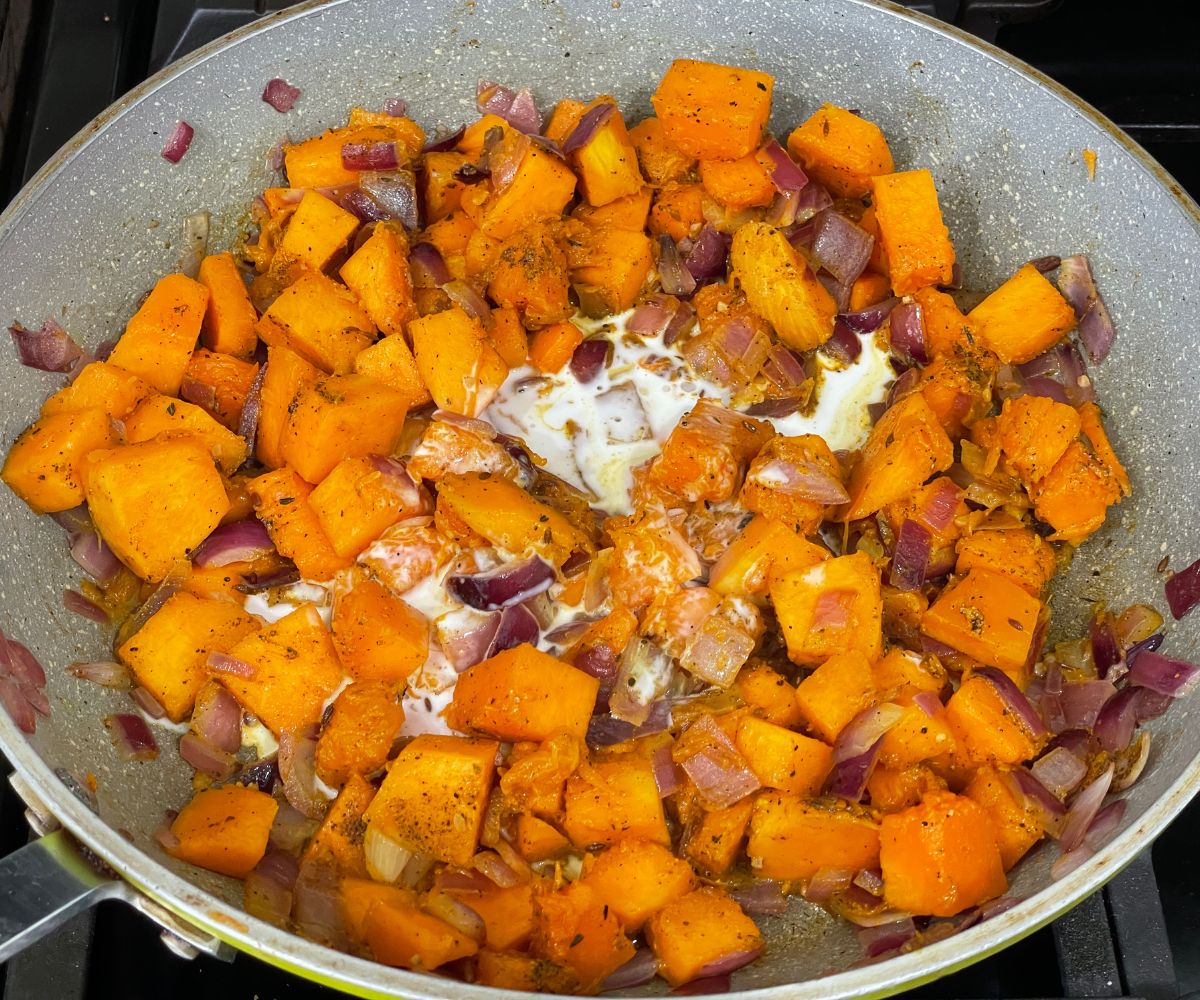 A pan is with spices, pumpkin and coconut milk over the flame.