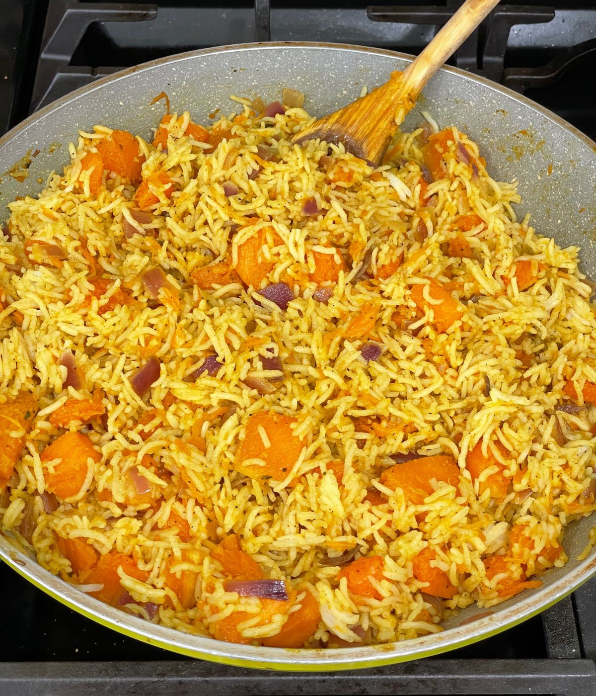 A non stick pan is with pumpkin rice and wooden spatula inserted.