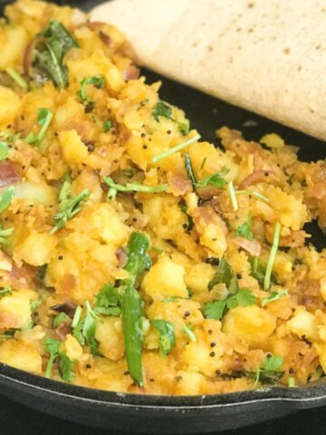 a cast iron skillet is filled with spicy potato curry.