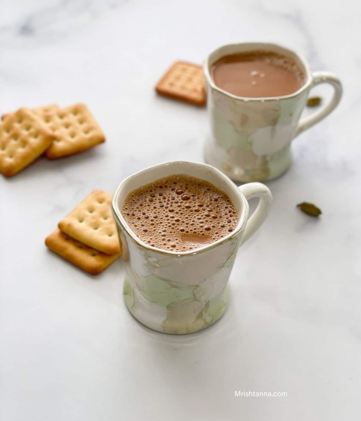 Two cups of vegan chai is on the table along with crackers.