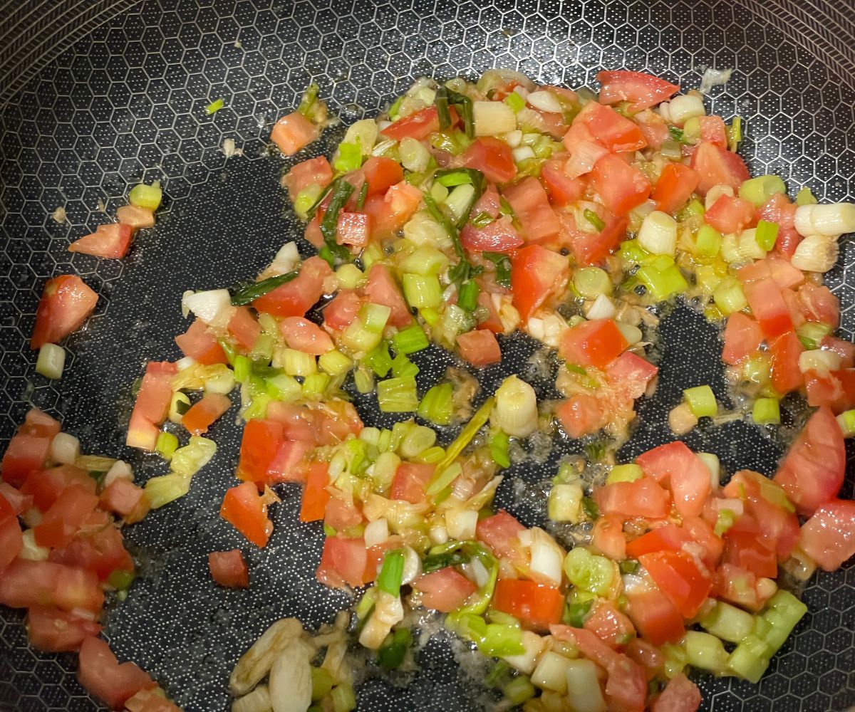 A pan is with onions and tomatoes over the heat.