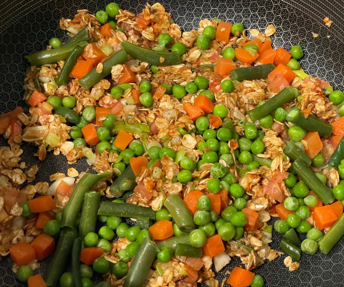 A pan has mixed vegetables and oats over the heat.
