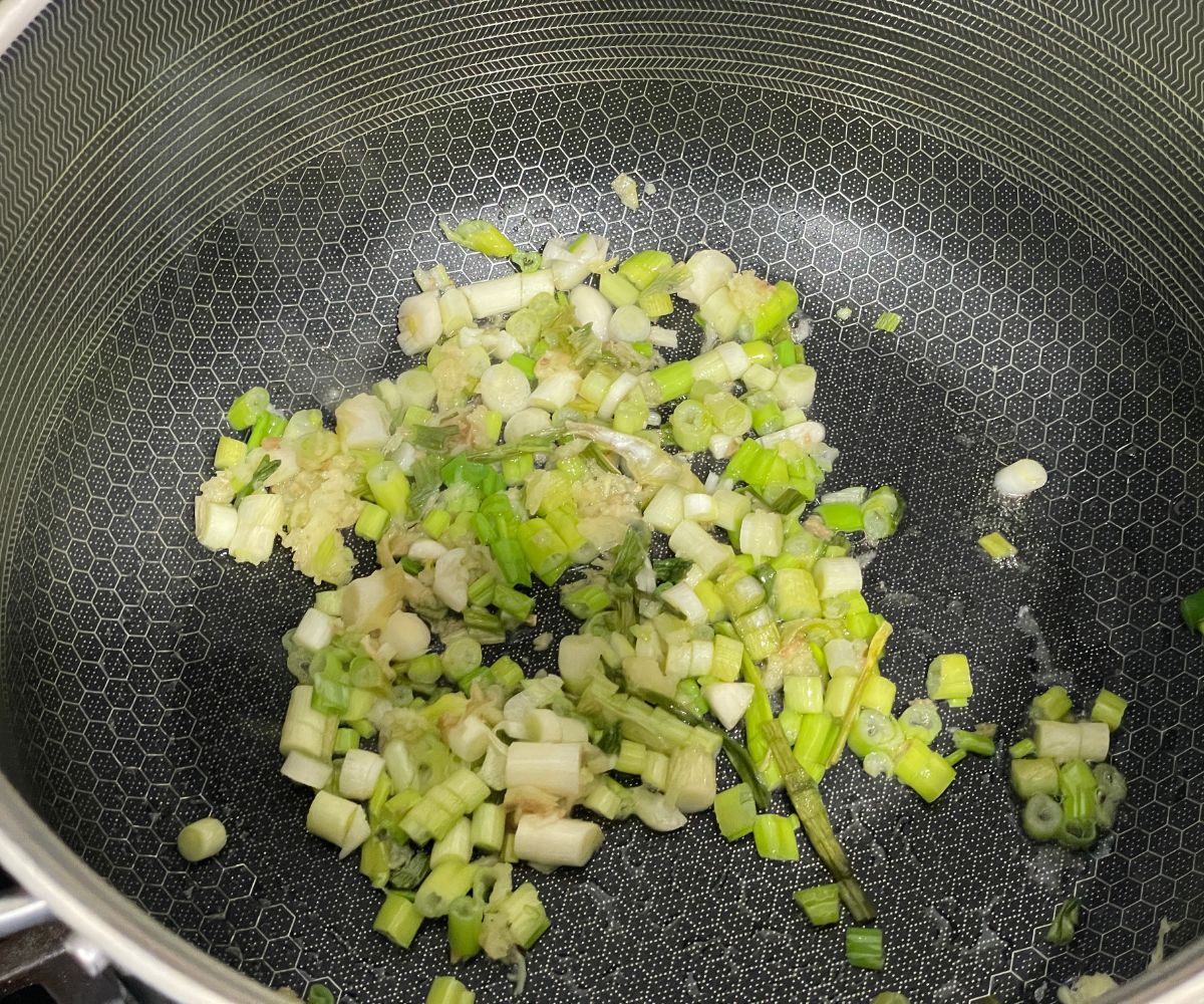 A pan has chopped green onions on the heat.