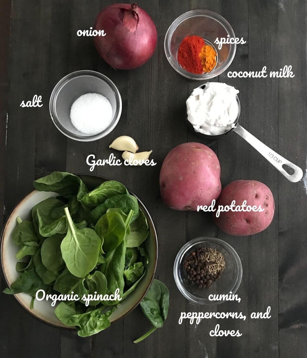 A table is filled with spinach soup ingredients like onion, spinach, and potatoes