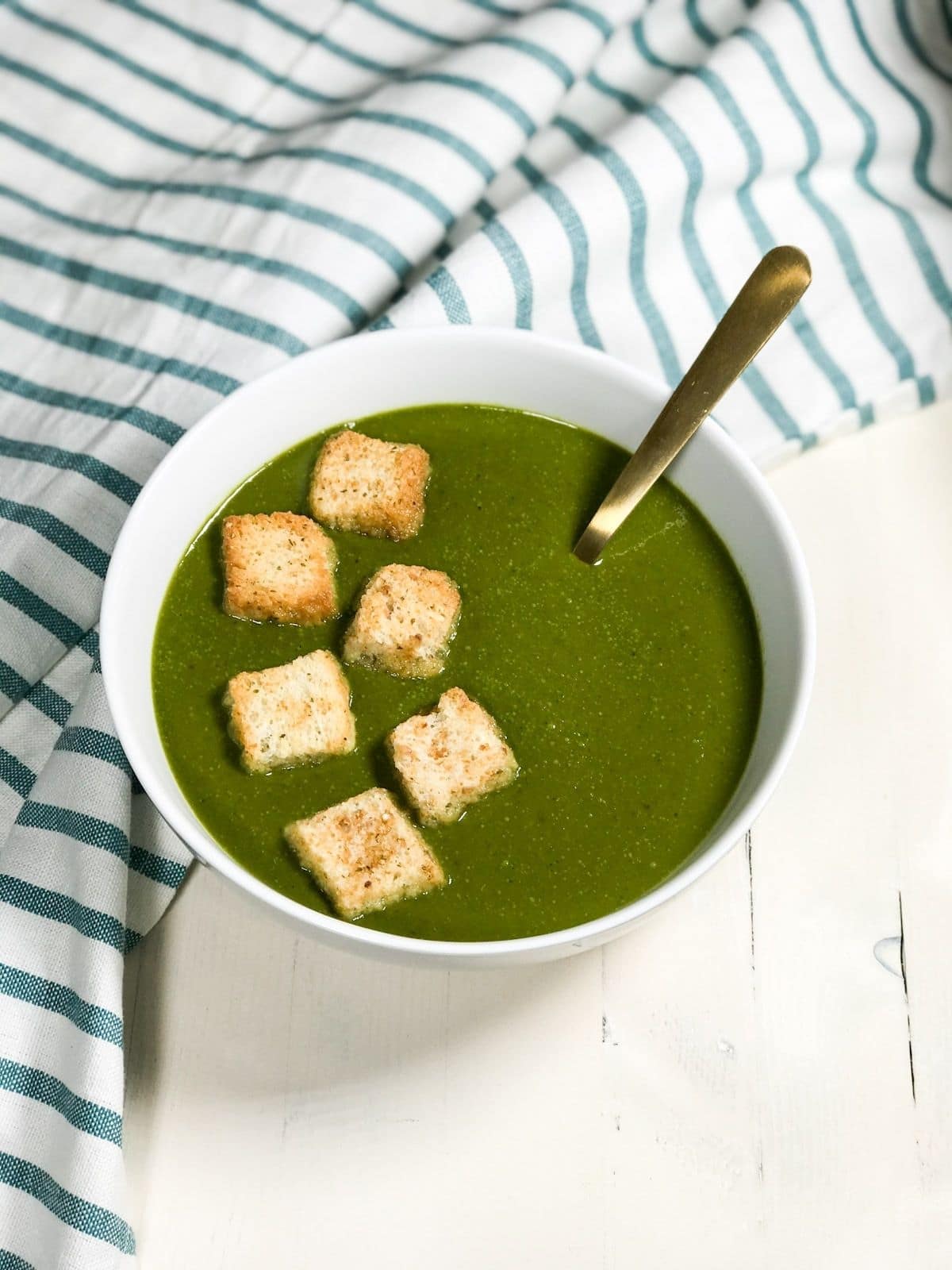 A bowl is filled with vegan spinach soup and a golden spoon is inserted