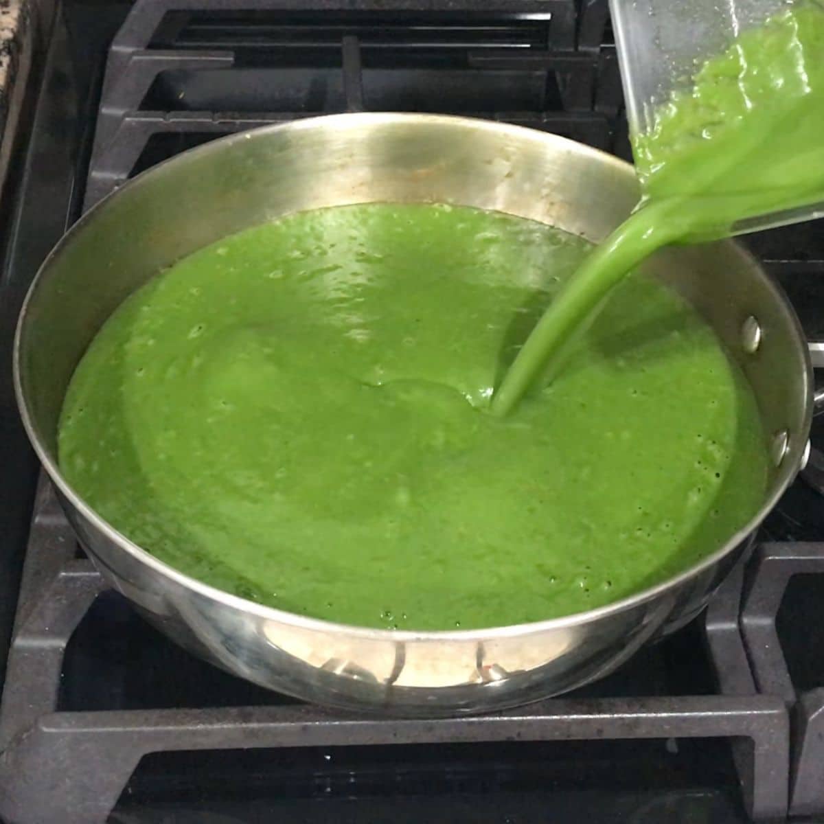 A pan is with spinach soup and its on the medium heat