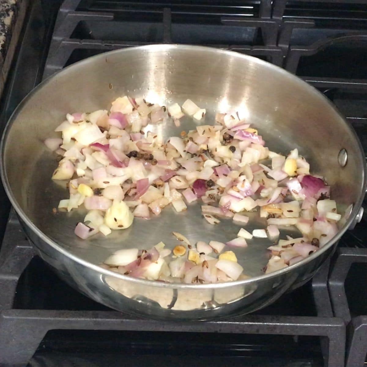 A pan is with spices and onions over the heat