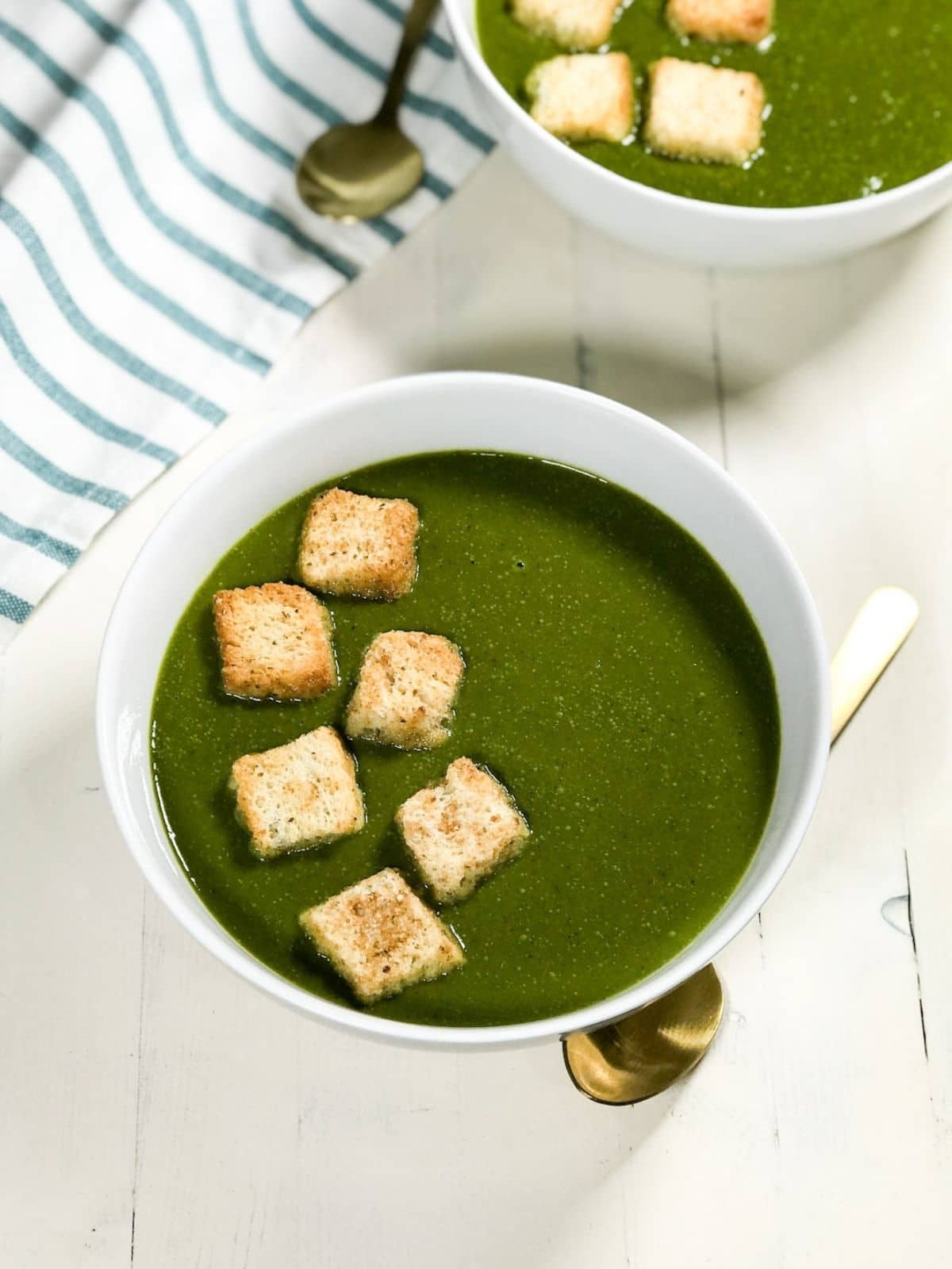 A bowl of spinach soup is on the table and topped with croutons.