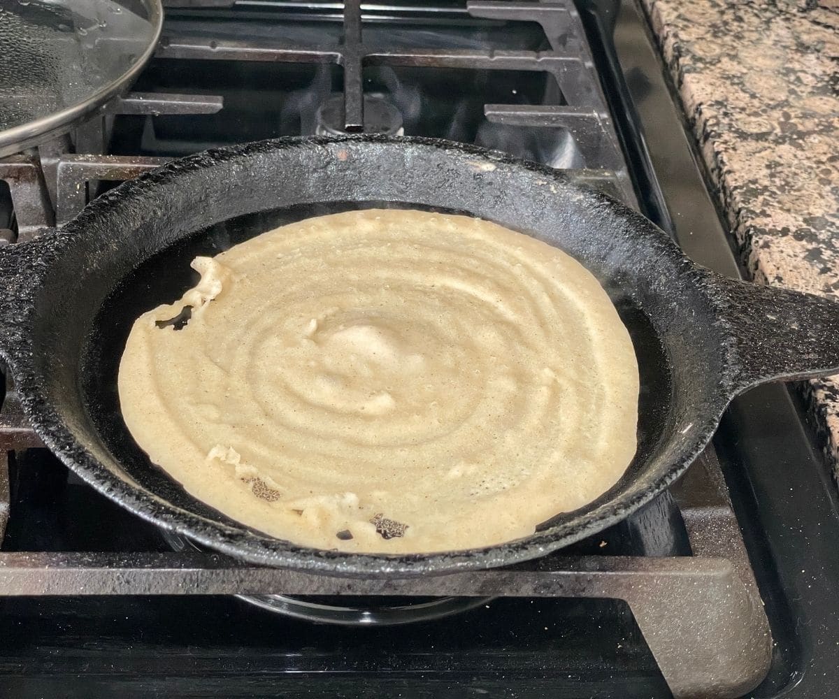 A cast iron skillet is with wheat dosa over the heat.