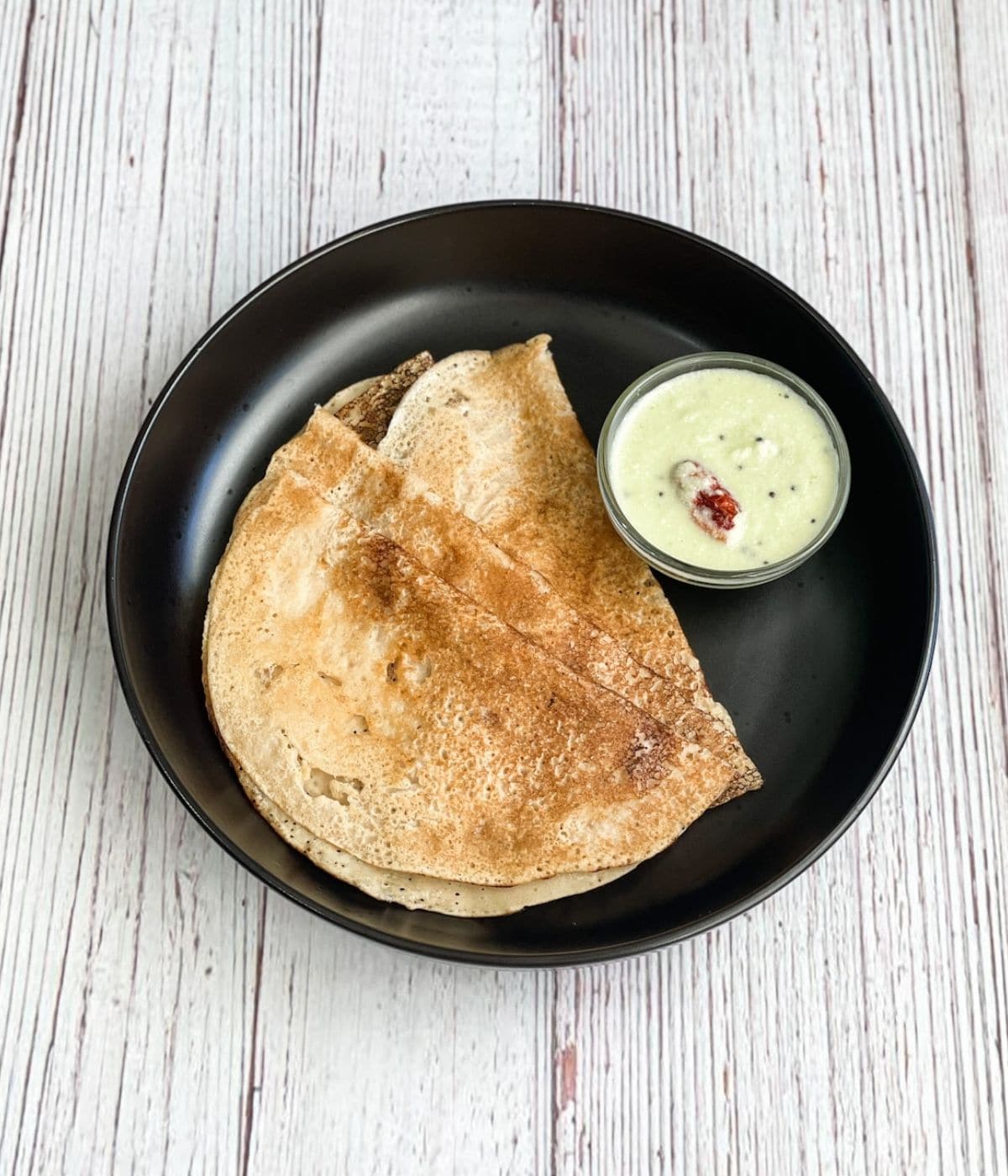 A plate of wheat dosa and chutney is on the table.