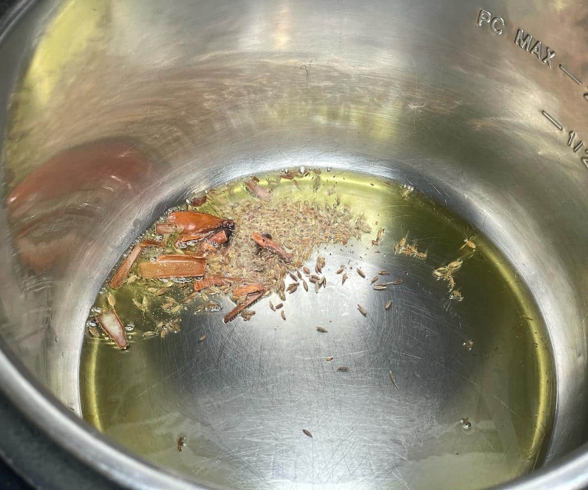 An instant pot is with oil, spices on saute mode.